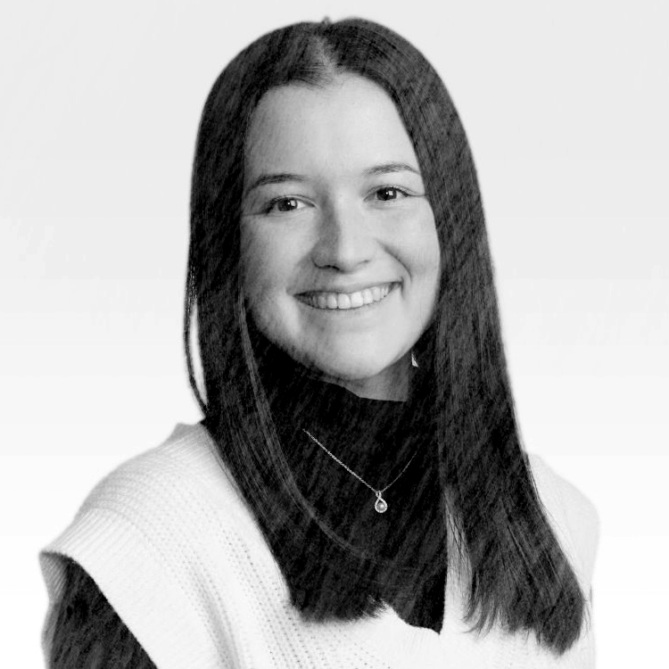 A black and white portrait of a smiling woman with long hair, wearing a sweater and a necklace.