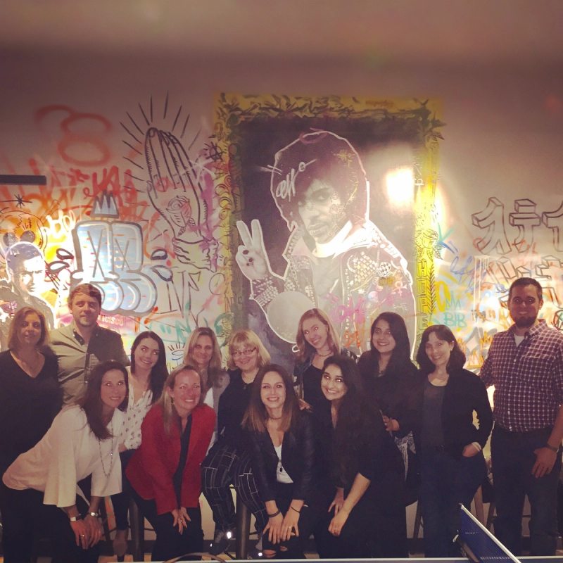 Employees pose in front a Prince and graffiti mural