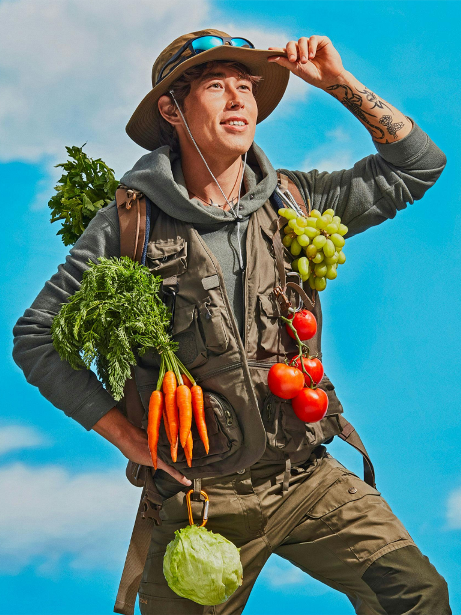 A person in hiking gear adorned with fresh produce under a clear blue sky.