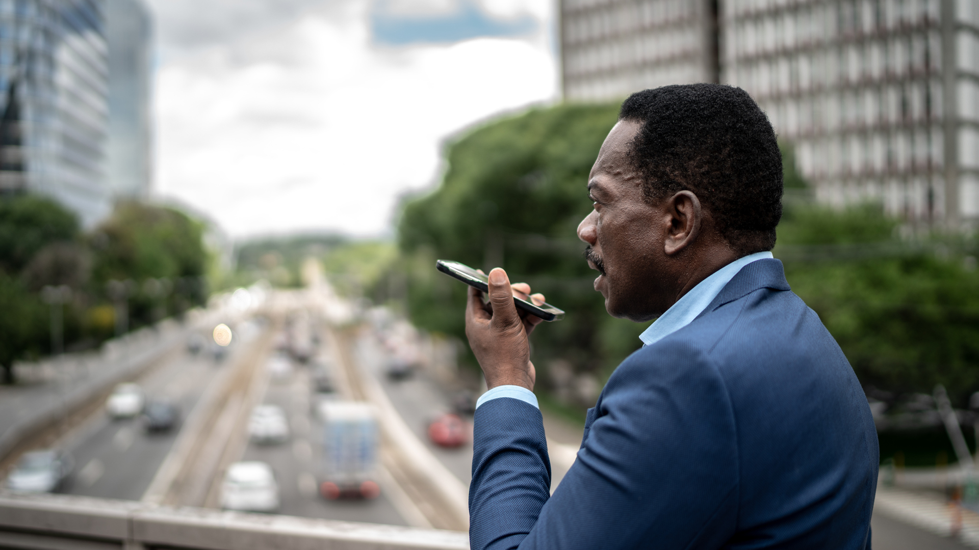 Man in suit using phone with city traffic in background.