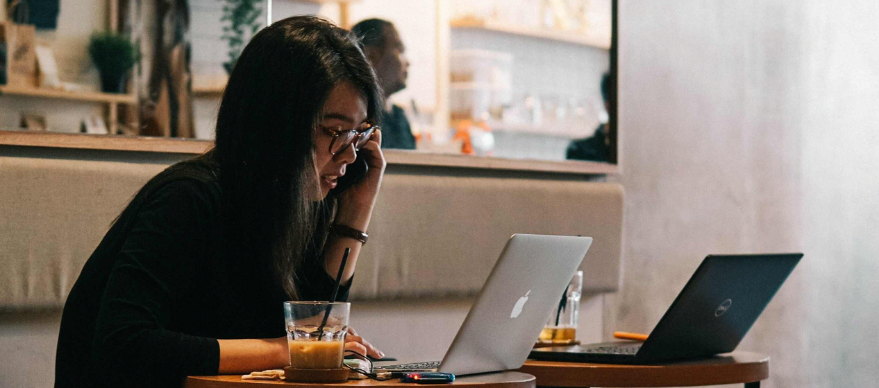 A person in a cafe working intently on a laptop with a beverage aside.