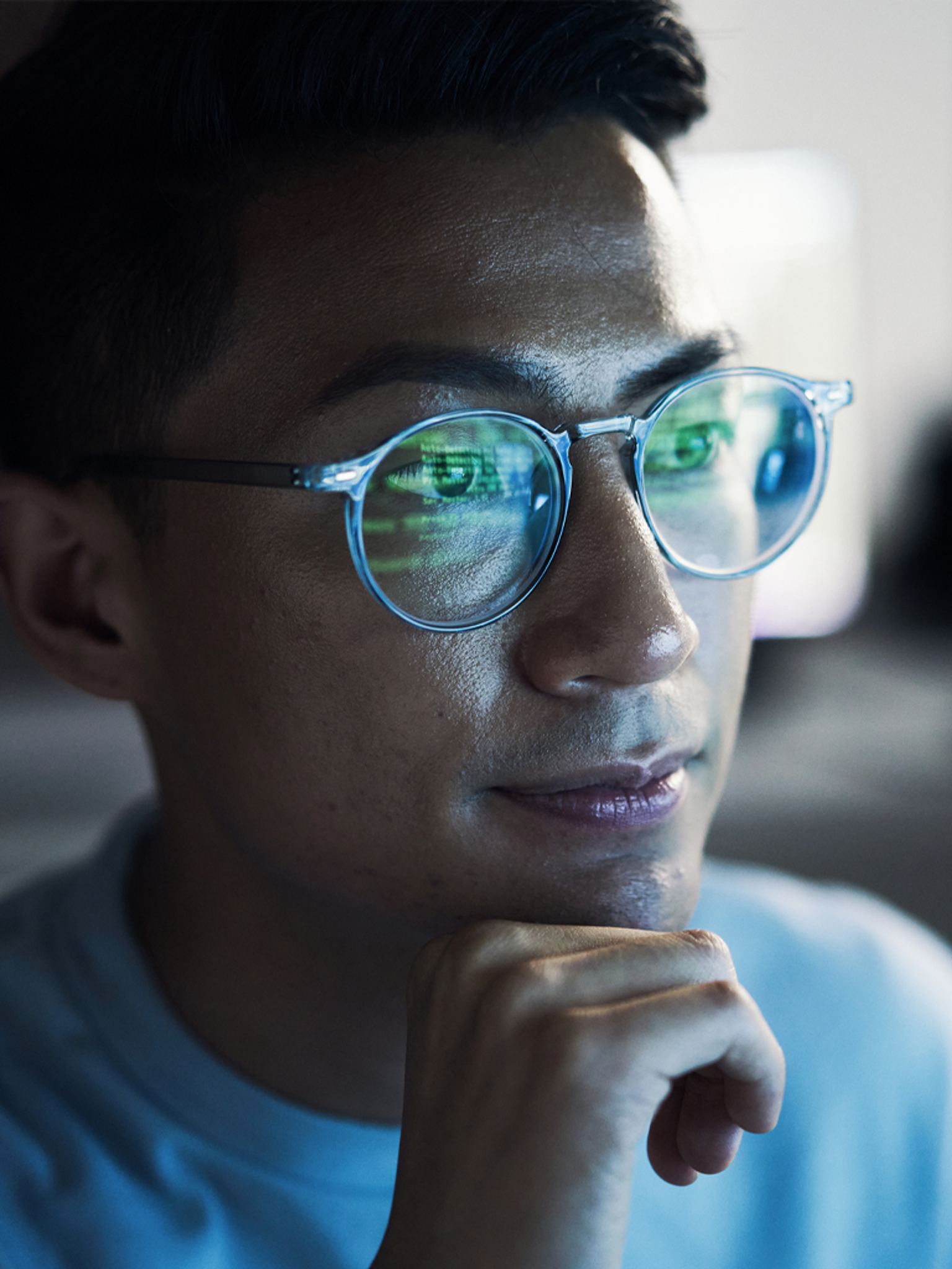Man with glasses reflecting a code screen, deep in thought.