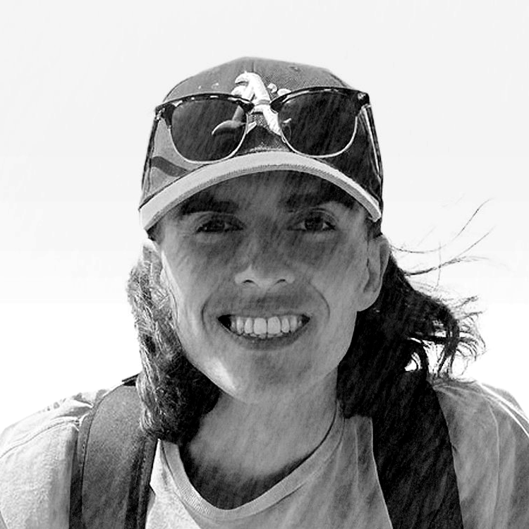 A person smiling, wearing a cap with sunglasses on top, in a black and white photo.