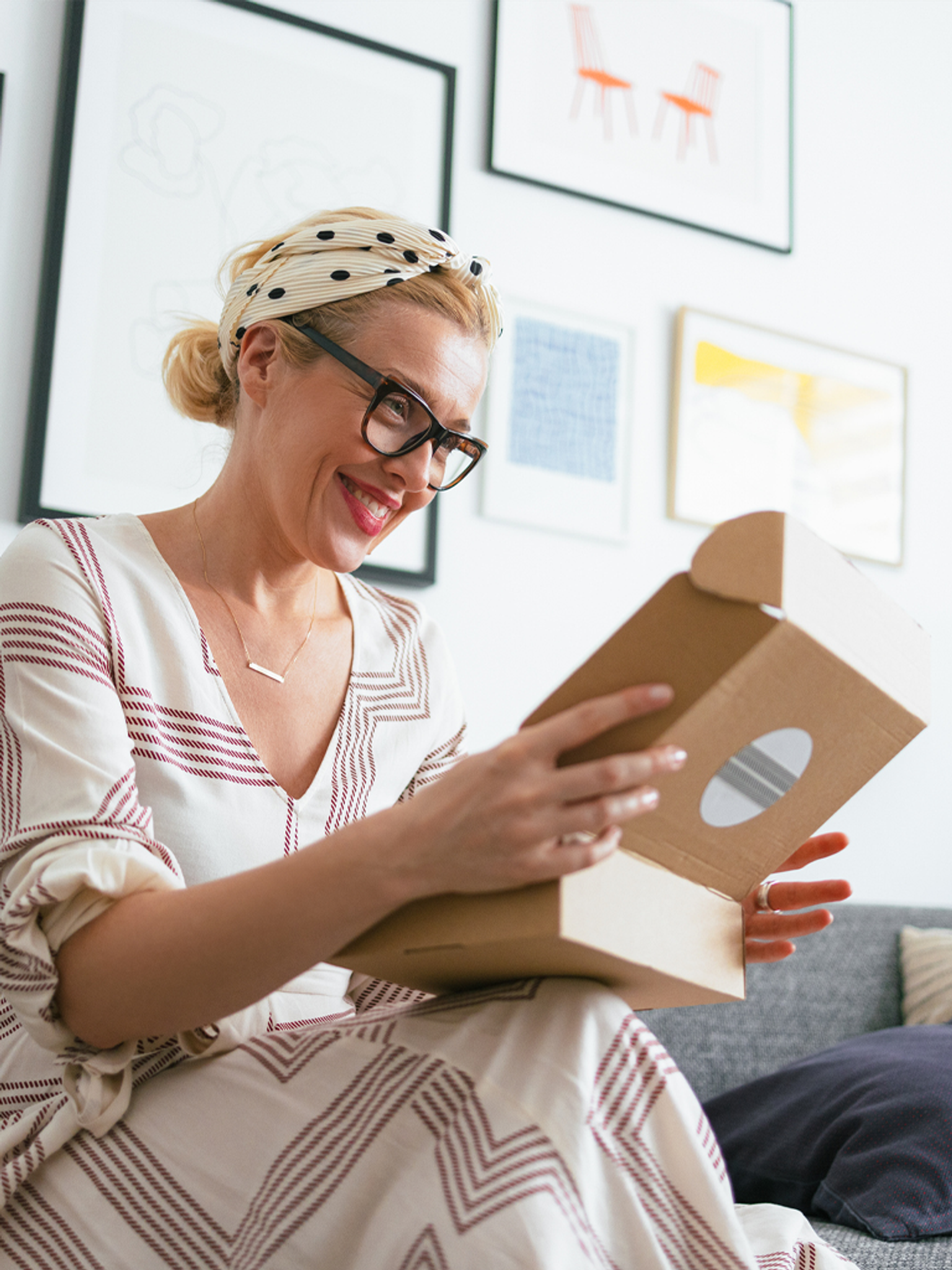 Smiling woman with glasses opens a package at home.
