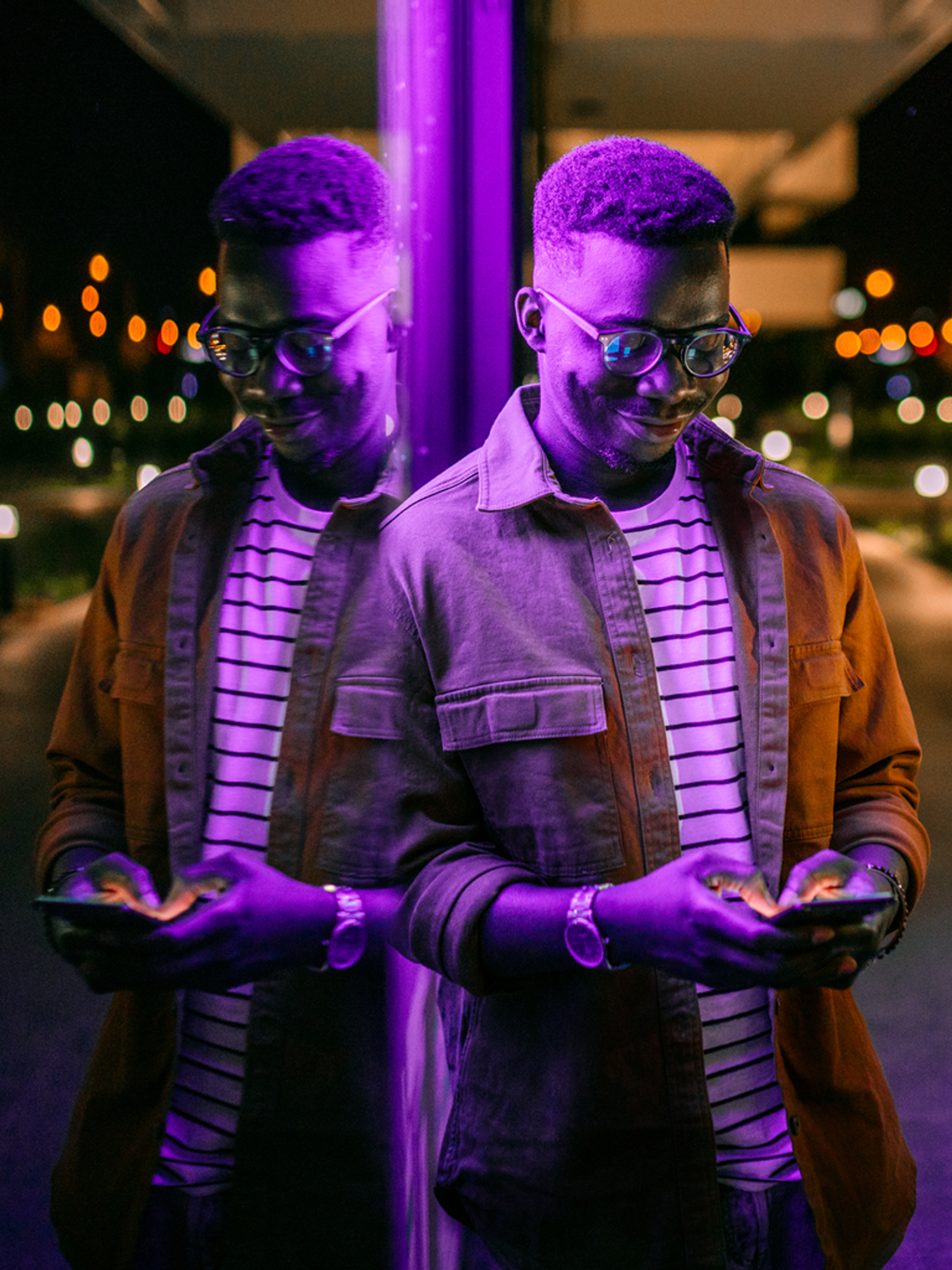 A person's double exposure portrait with neon purple lighting, looking at a smartphone at night.
