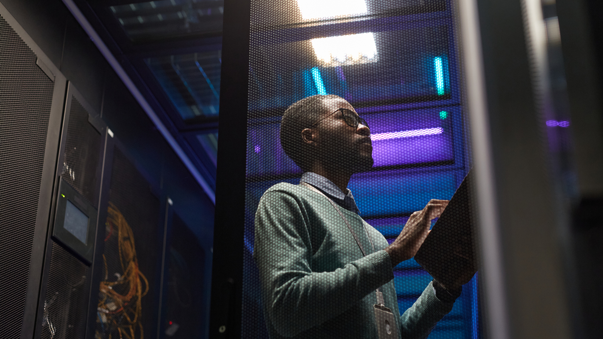 A person with a clipboard inspects a server room, illuminated by blue lights.
