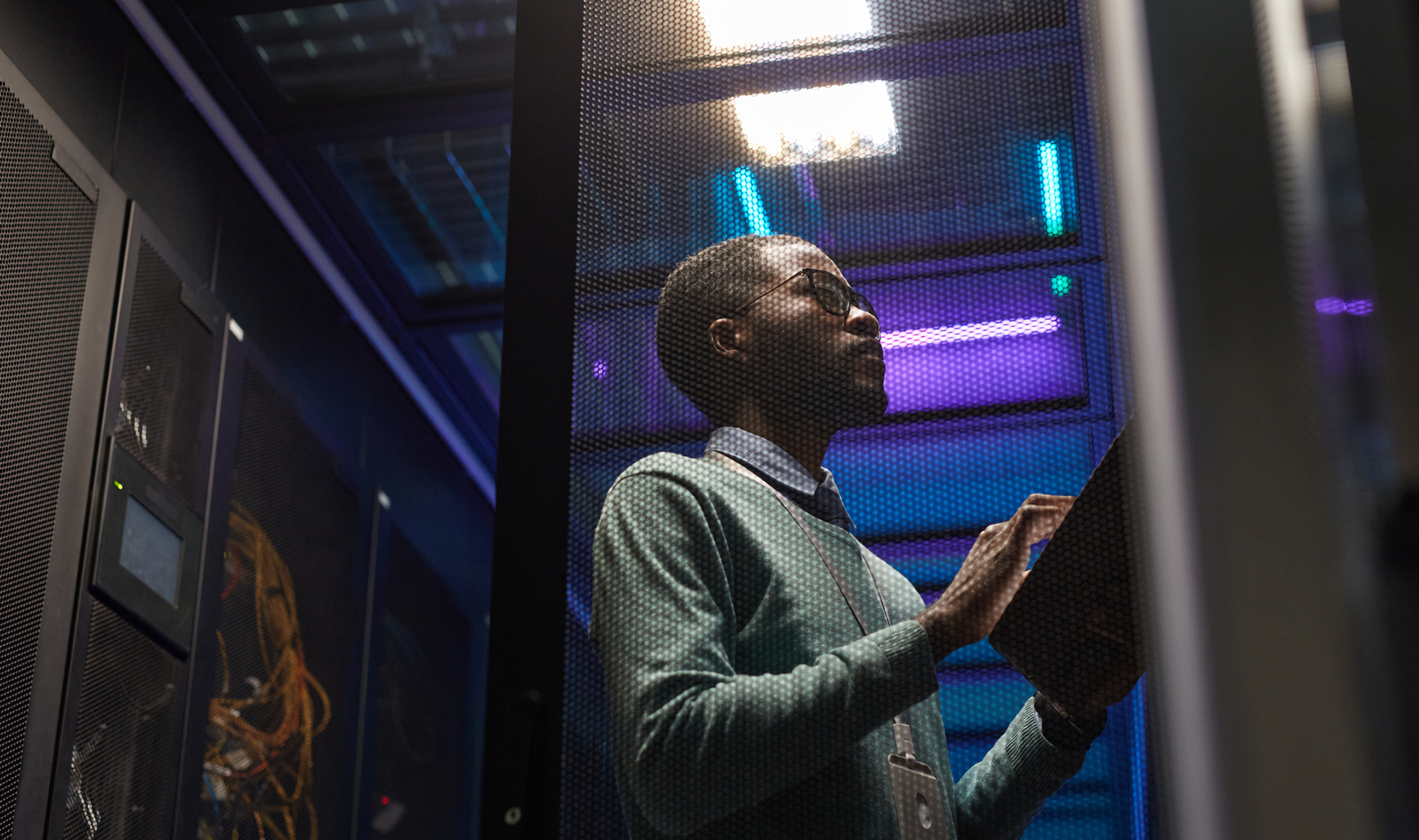 A person with a clipboard inspects a server room, illuminated by blue lights.